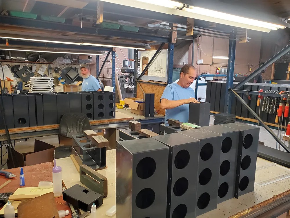 Workers assembling black fabricated enclosures in an industrial workshop